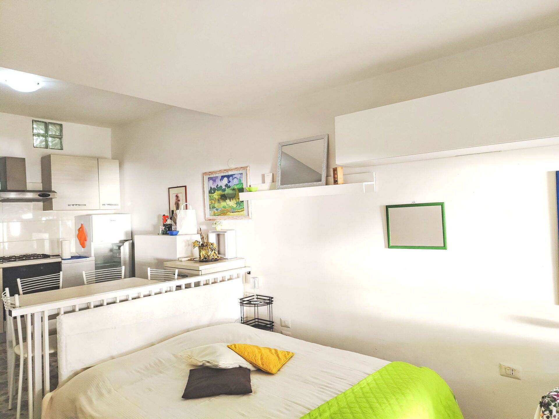 A hotel room with a bed, a small desk, a chair, a kitchenette, and a mirror.