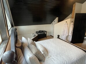 A bedroom with a bed, pillows, a nightstand, a mirror, and a staircase leading to an upper level.