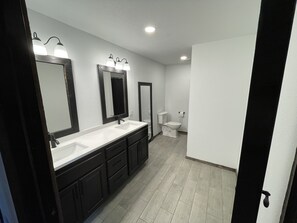 A modern bathroom with a double sink vanity, a toilet, and a mirror with lights.