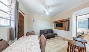 A modern room with a bed, a sofa, a TV mounted on a wooden panel, and a ceiling fan.