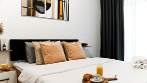 A neatly made bed with a tray of breakfast items, a bedside table with a cup and glasses, and a wall art piece above the bed. - Sandra (Bucharest)