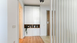 A hallway with a wooden floor leading to a white cabinet with a plant and a small shelf. - Sandra (Bucharest)
