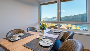 Un coin repas avec une table dressée pour quatre personnes, une vue sur les montagnes et un lac, ainsi qu’un luminaire moderne au plafond.