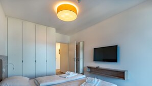 Une chambre d’hôtel moderne équipée de deux lits, d’un téléviseur à écran plat, d’une étagère intégrée et d’un luminaire au plafond.