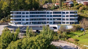 Un hôtel à plusieurs étages, doté d’un design moderne, situé dans une région montagneuse, entouré de verdure et de maisons.