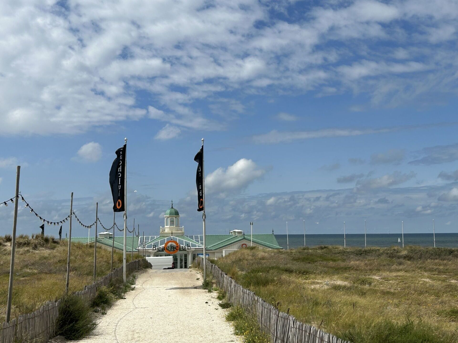 A pathway leading to a building with a green roof and a tower, surrounded by flags and a fence.
