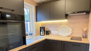 Moderni keittiö, jossa on sisäänrakennettu uuni, kahvinkeitin, pyöreä peili ja puiset kaapit.