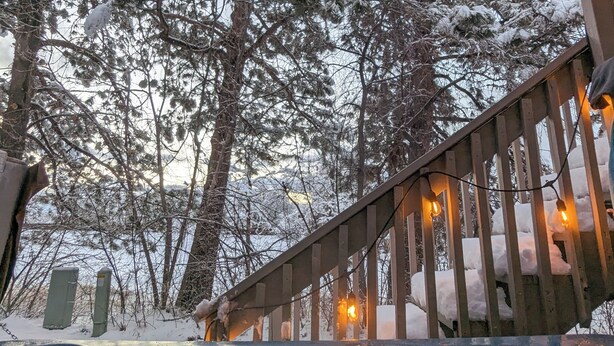 Eine Holzterrasse mit Whirlpool, umgeben von schneebedeckten Bäumen.