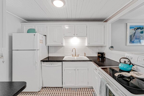 A kitchen with white cabinets, a black countertop, a sink, a stove, and a teal kettle. - 🌊 Direct Oceanfront 2/2 | Private Balcony | Heated Beachfront Pool ♨️ & Beach Access (New Smyrna Beach)