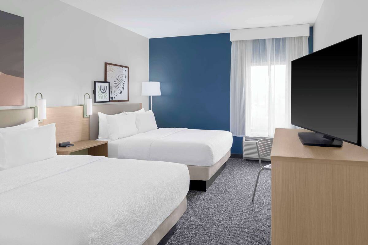 A hotel room with two beds, a TV, a desk, and a window with curtains.