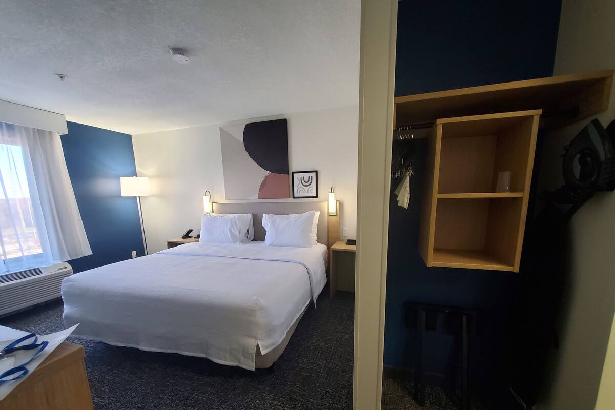 A hotel room with a large bed, bedside tables, a desk, a chair, a coat rack, and a wardrobe.