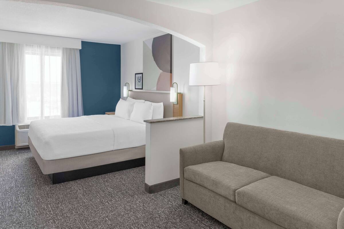 A hotel room with a bed, a sofa, a desk, and a large mirror.