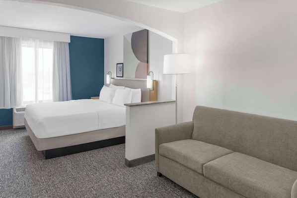 A hotel room with a bed, a sofa, a desk, and a large mirror. - Spark by Hilton Lansing (Lansing)
