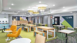 A modern indoor space with multiple tables and chairs, a vending machine, and a wall with a geometric design and the word "spark". - Spark by Hilton Lansing (Lansing)
