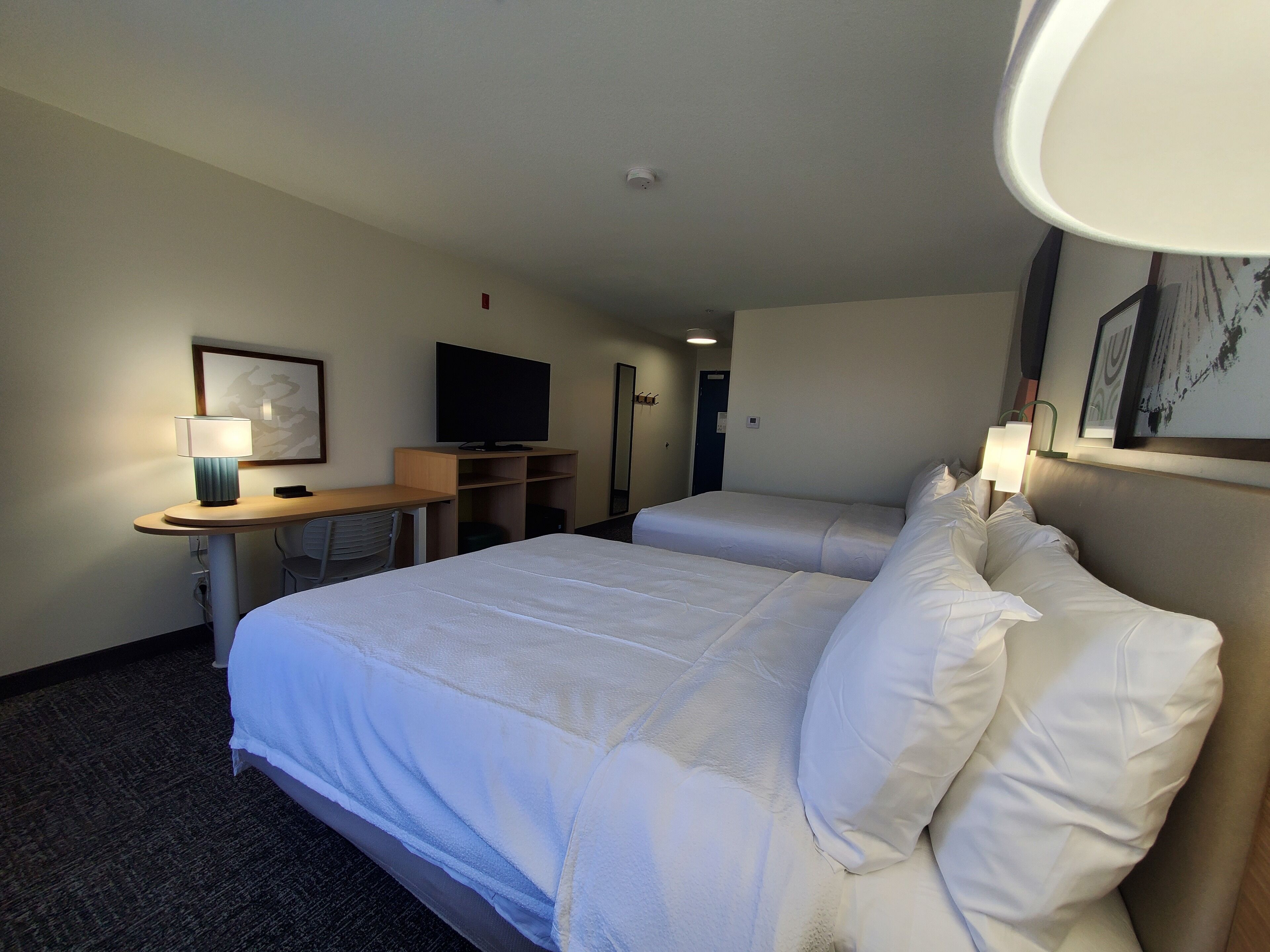 A hotel room with a large bed, a desk with a lamp, a television, and a framed picture on the wall.