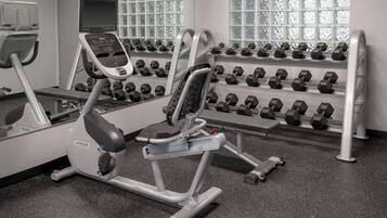 A gym with cardio equipment, dumbbells, and a mirrored wall.