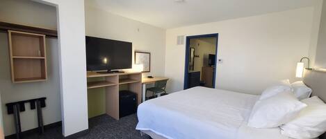 A hotel room with a bed, a desk, a television, a wardrobe, and a bathroom visible through an open door.