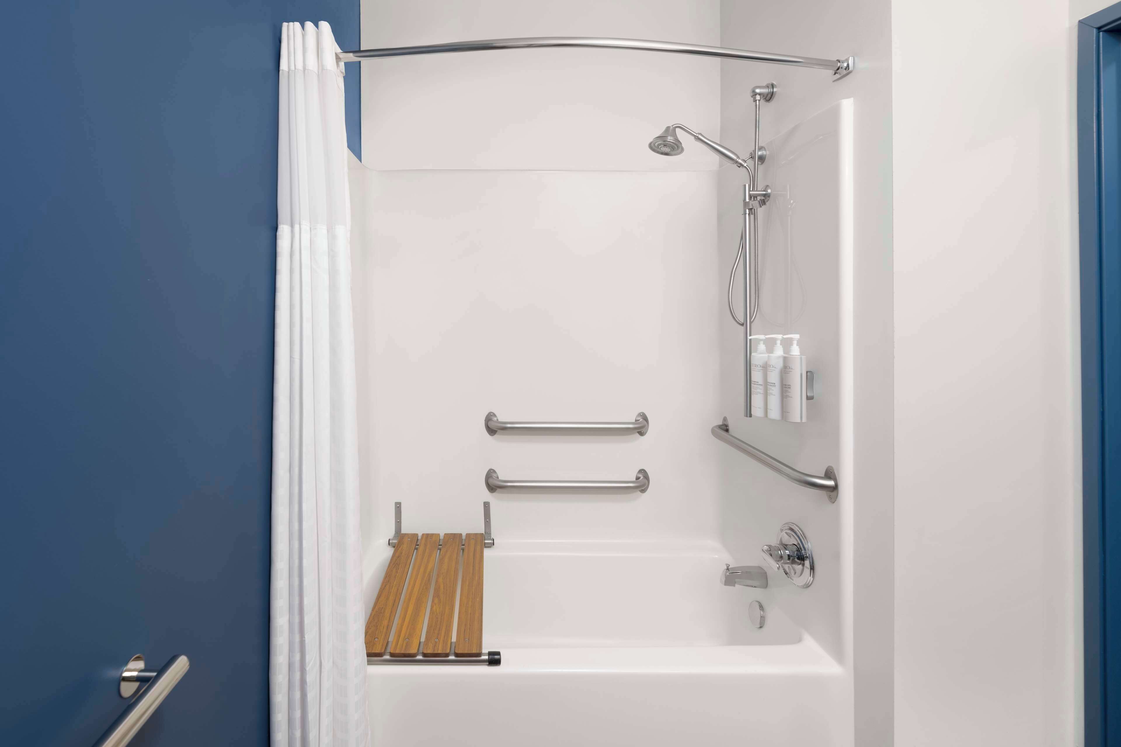 A modern bathroom with a bathtub, shower, and handrails.