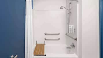 A modern bathroom with a bathtub, shower, and handrails.