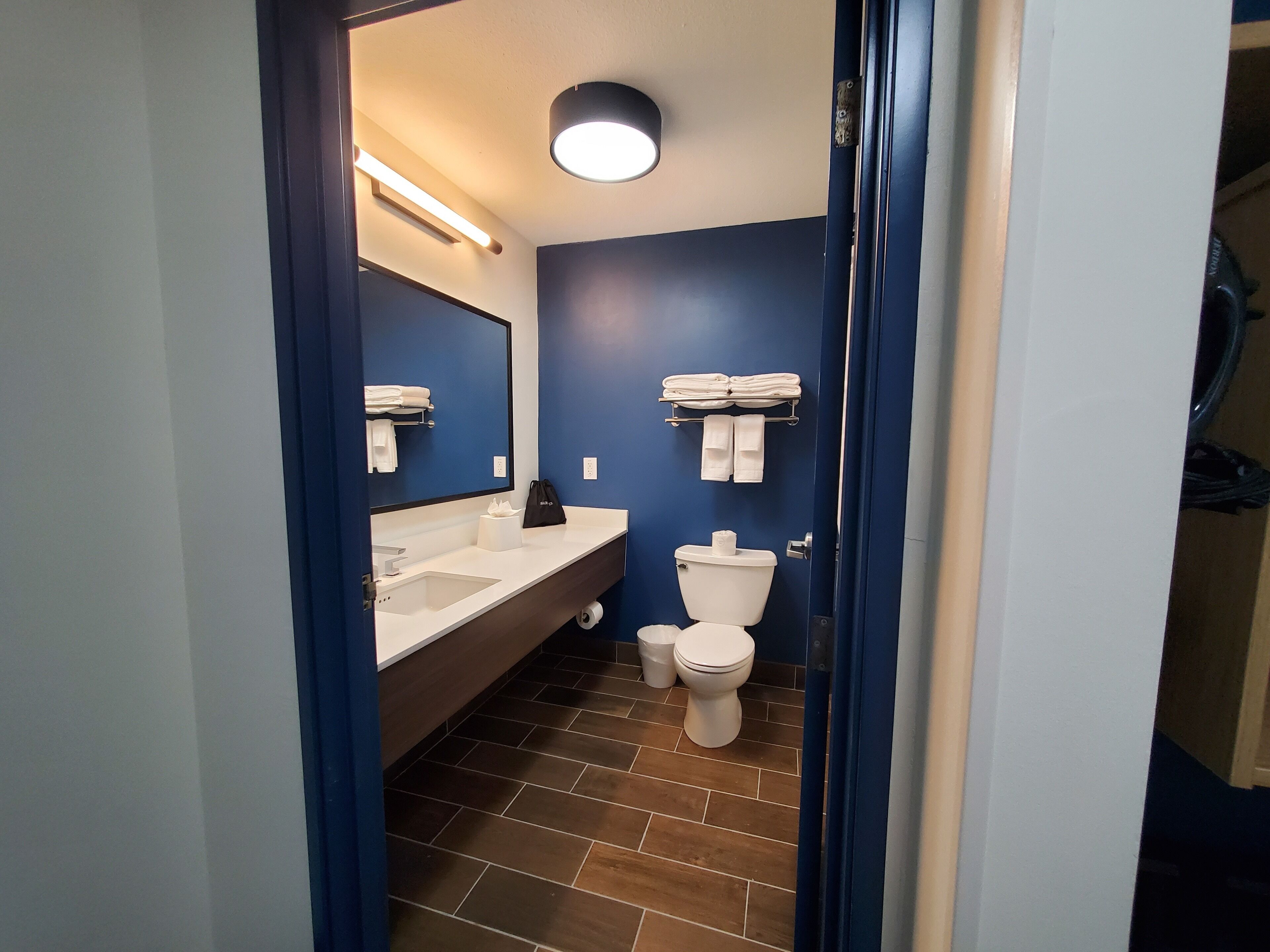 A modern bathroom with a white sink, a toilet, and a mirror. There are towels hanging on a rack above the toilet.