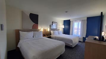 Habitación de hotel con dos camas, un escritorio, un televisor y una ventana con cortinas.