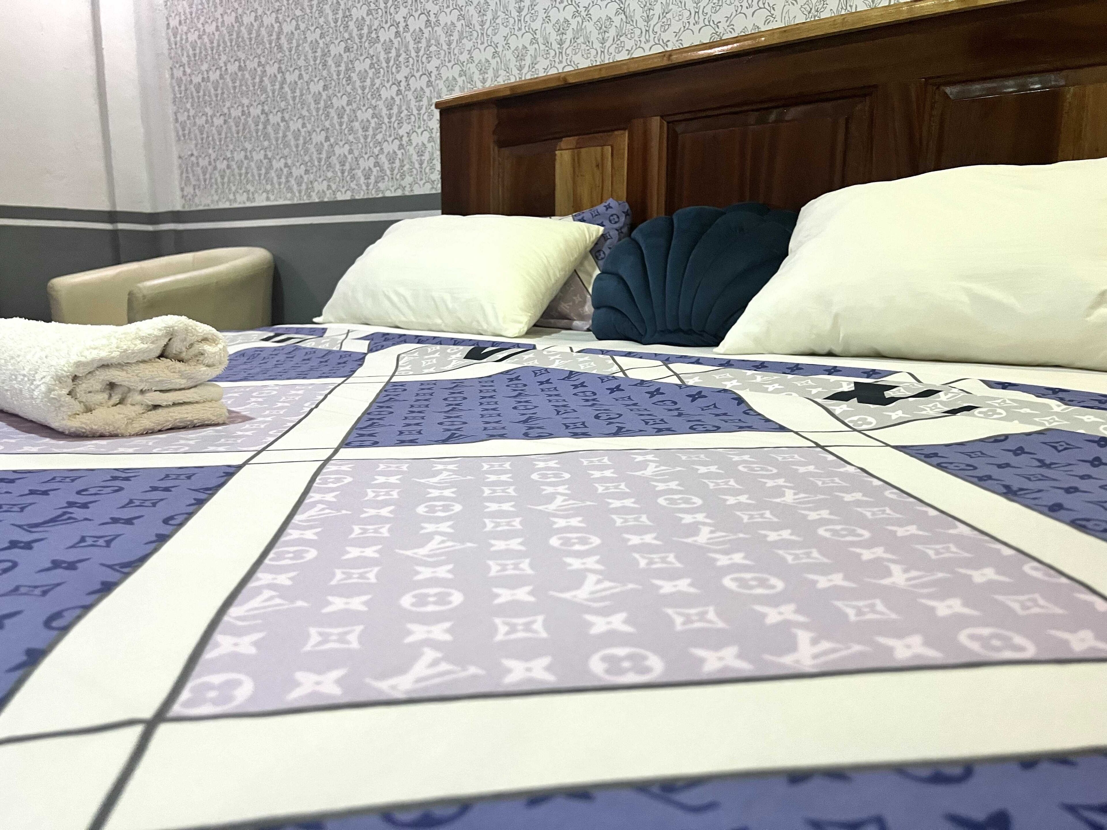 A hotel room with a neatly made bed, a wooden headboard, and a patterned bedspread.
