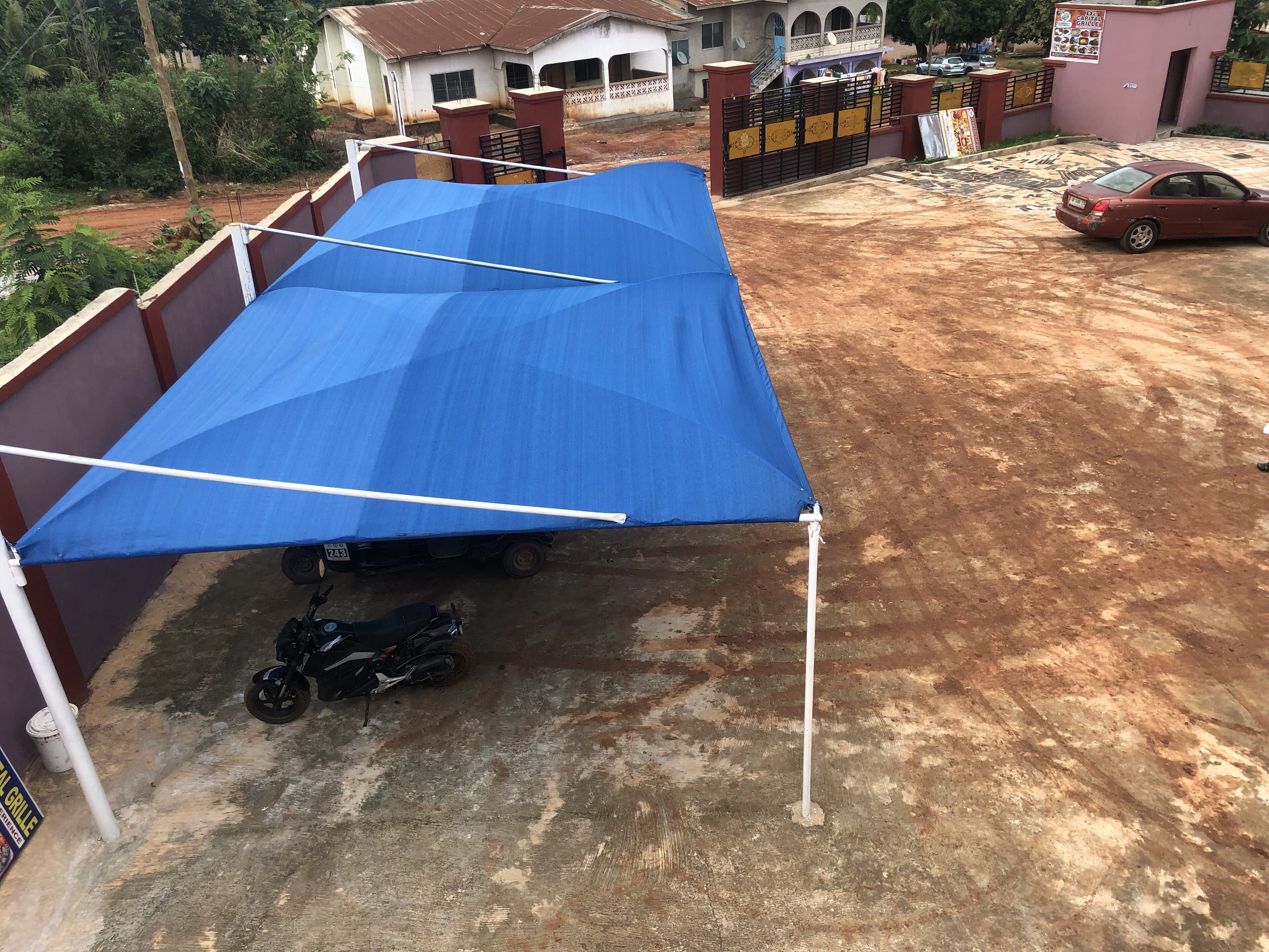 A blue canopy over a motorcycle, a dirt ground, and a gated entrance to a building.