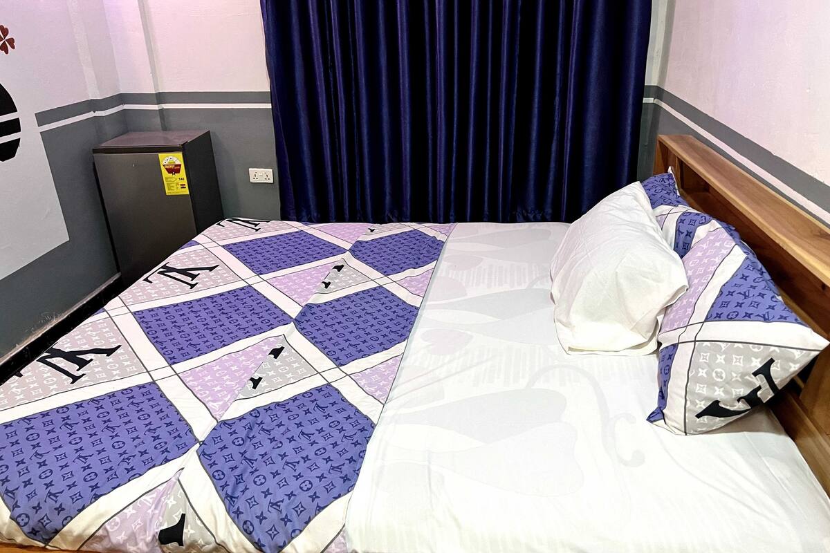 A neatly made bed with a patterned bedspread, a wooden headboard, and a single pillow.