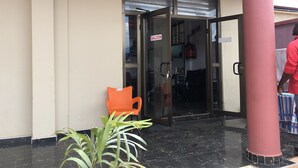 A hotel entrance with a glass door, an orange chair, and a potted plant. - De Capital Hotels & Restaurants (Goaso)