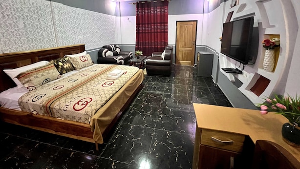 A hotel room with a bed, a desk, a TV, and a door. - De Capital Hotels & Restaurants (Goaso)