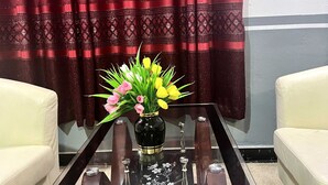 A room with a glass-top coffee table, a vase with flowers, and two white sofas. - De Capital Hotels & Restaurants (Goaso)