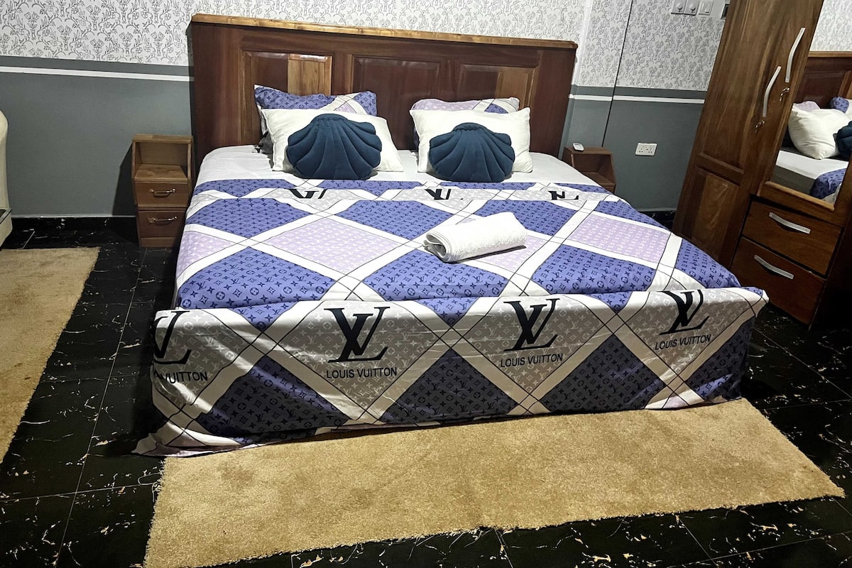 A bed with a Louis Vuitton quilted bedspread, a wooden headboard, and a brown rug.