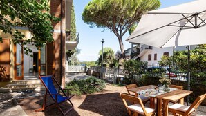 Un patio al aire libre con una mesa y sillas, rodeado por un jardín y un árbol.