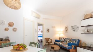 Un espacio habitable amplio y luminoso con comedor, sofá y vista al mar a través de una puerta abierta.