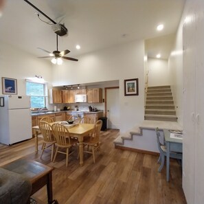 Een moderne keuken met houten kasten, een eethoek met een tafel en stoelen, een plafondventilator en een trap naar een ander niveau.