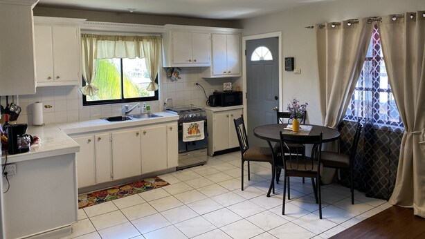 A compact kitchen with white cabinets, a stove, a sink, and a dining area with a table and chairs.