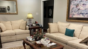 A living room with two beige sofas, a wooden coffee table, a patterned rug, and a framed artwork on the wall. - Great Masters rental, walking distance to the tournament. (Augusta)