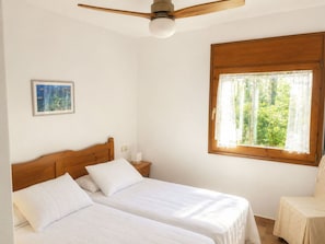 A bedroom with two beds, a ceiling fan, a window with lace curtains, and a framed picture on the wall.