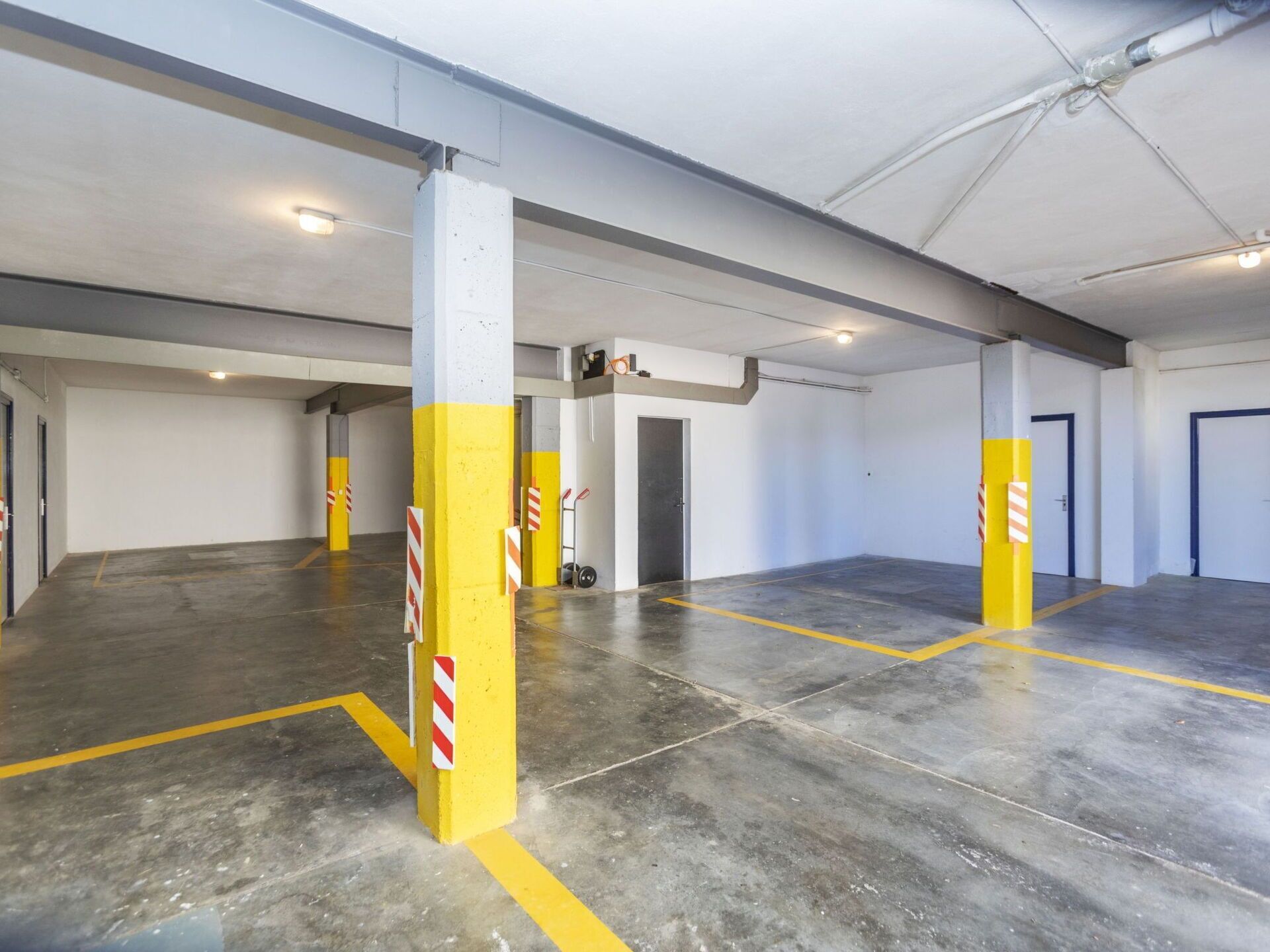 A spacious indoor parking area with concrete floors and yellow pillars marked with red and white stripes.