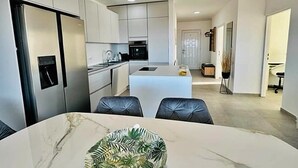 Une cuisine moderne avec des meubles blancs, un îlot central et un coin repas doté d’une table en marbre.