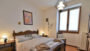 Un dormitorio con cama de madera, dos mesitas de noche, una lámpara de pared e imagen enmarcada.