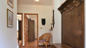Un pasillo con suelo de madera, una silla de mimbre, un armario de madera y una puerta que da a otra habitación.