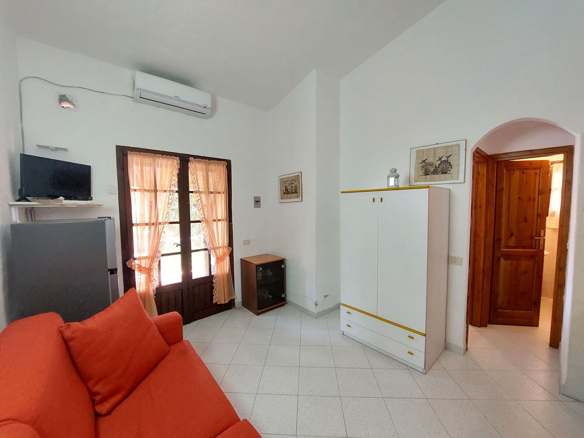 Un espacio habitable pequeño con sofá, televisor, armario y una puerta que da a otra habitación.