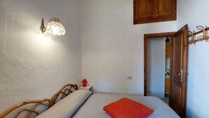 Une chambre à coucher avec un lit, une table de chevet, une lampe rouge, un luminaire fixé au mur et une porte en bois.