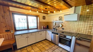 A kitchen with white cabinets, a dishwasher, an oven, and a sink. There is a window with curtains, a clock on the wall, and a tiled backsplash.