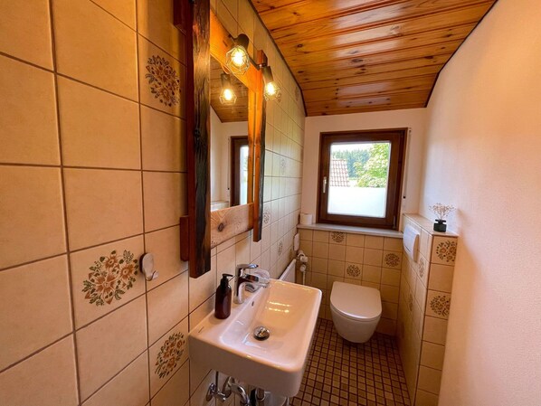 A compact bathroom with a wooden ceiling, a sink, a toilet, and a window with a view of the outside.