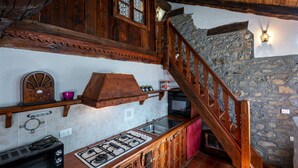 A rustic kitchen with wooden cabinets, a stone wall, and a wooden staircase. - Lovely apartment for 4 people with WIFI, TV and pets allowed (Avise)