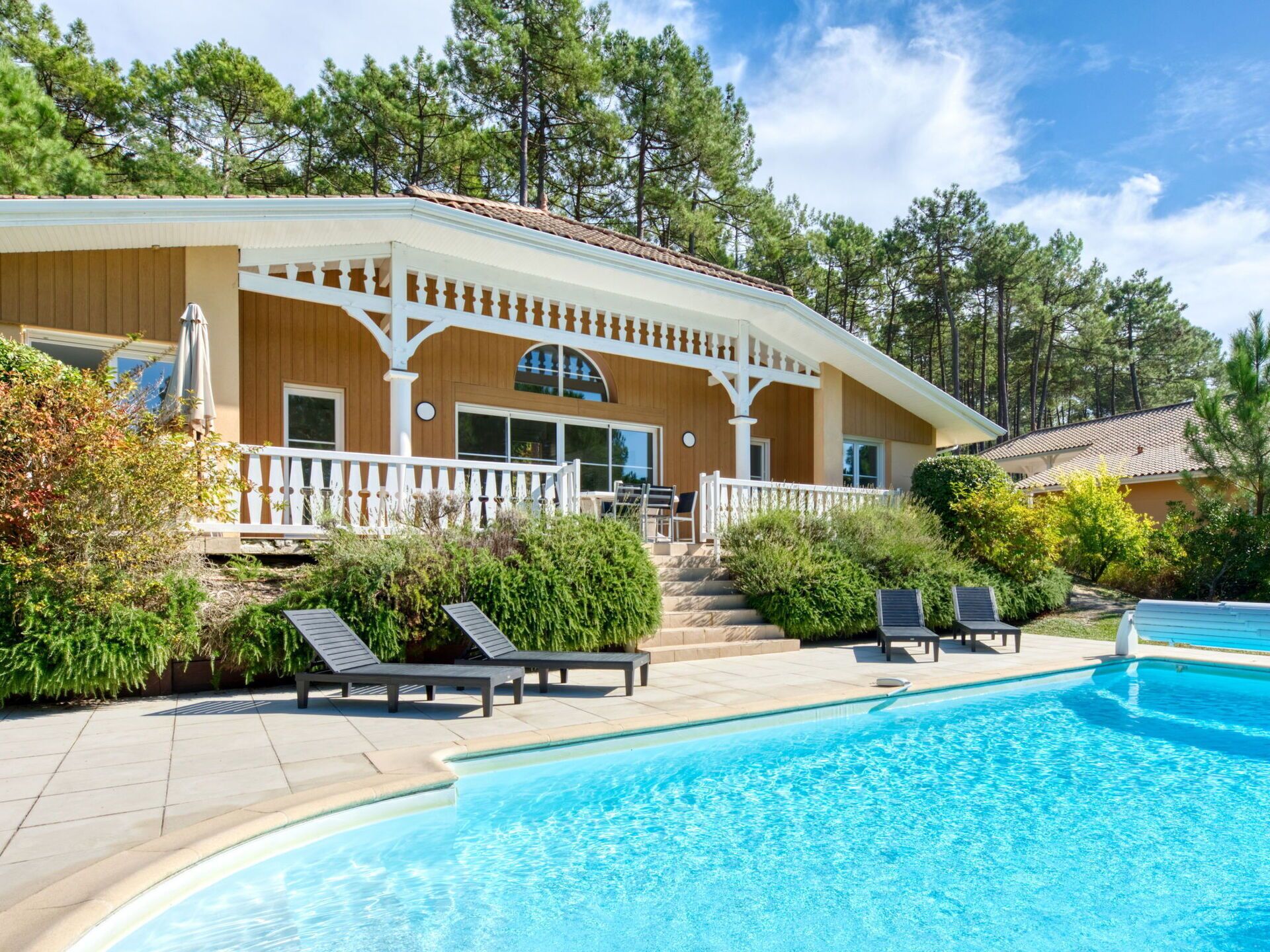 A two-story house with a pool, surrounded by trees and a white fence.