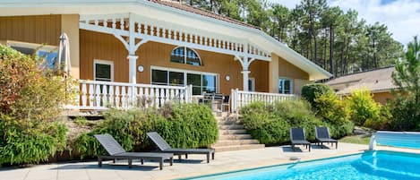 A two-story house with a pool, surrounded by trees and a white fence.
