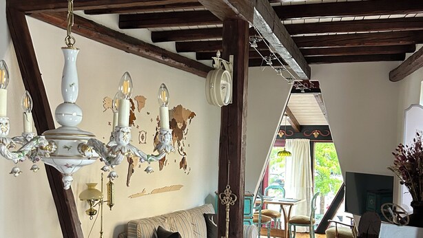 Un salon chaleureux avec un plafond en bois, un fauteuil bleu, un canapé à rayures et un mur décoratif agrémenté d’une horloge et d’œuvres d’art.